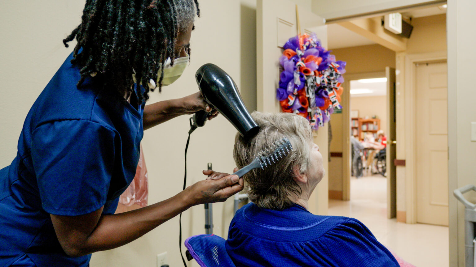 A woman is getting her hair done by a stylist at a salon in a skilled nursing facility