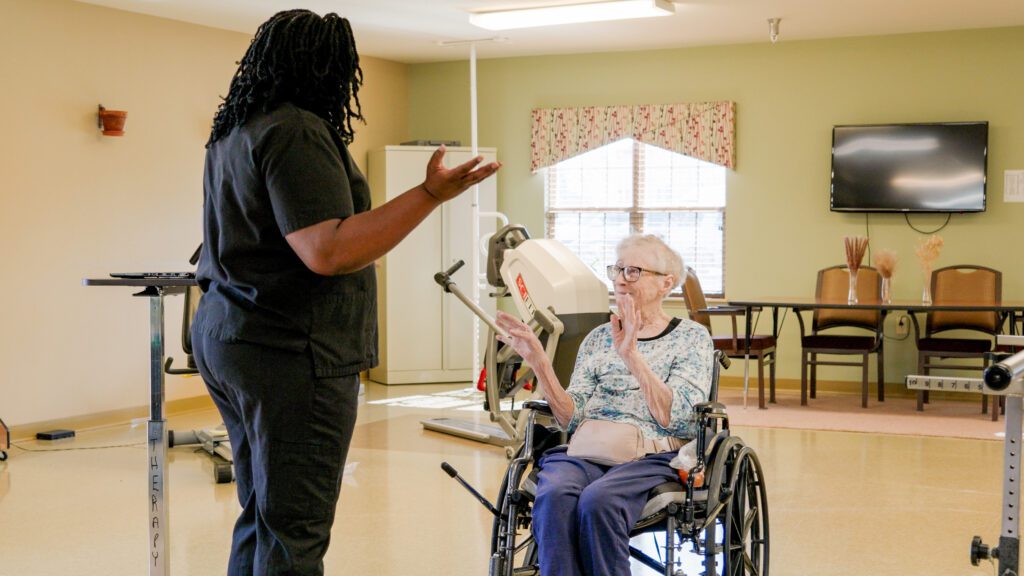 A woman in a wheel chair is assisted by a nurse in a short term care facility