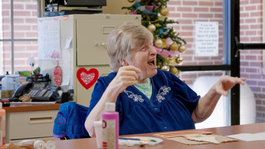 A woman smiles as she paints in a skilled nursing facility
